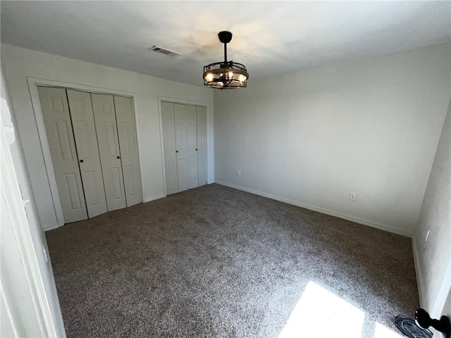 unfurnished bedroom featuring two closets, carpet flooring, baseboards, a chandelier, and visible vents