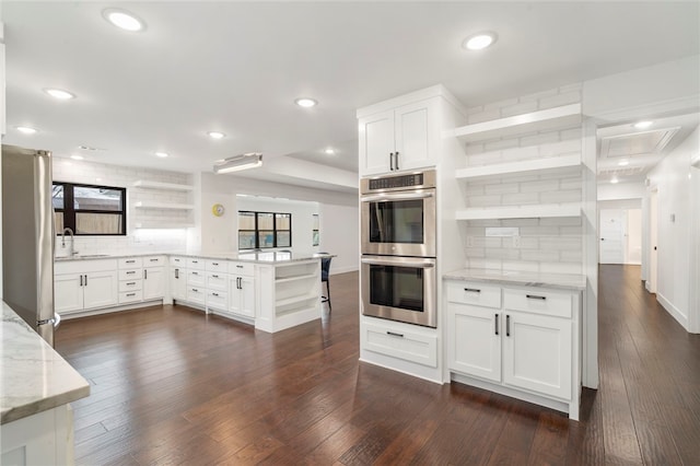 kitchen with white cabinets, decorative backsplash, light stone counters, kitchen peninsula, and stainless steel appliances