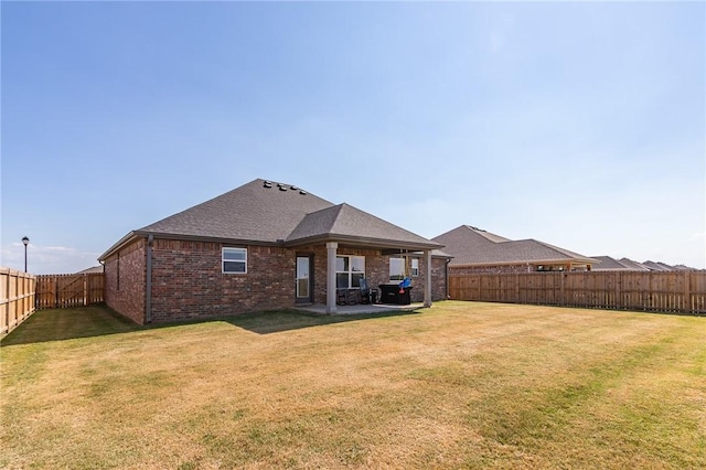 rear view of property with a patio, a fenced backyard, brick siding, a yard, and roof with shingles