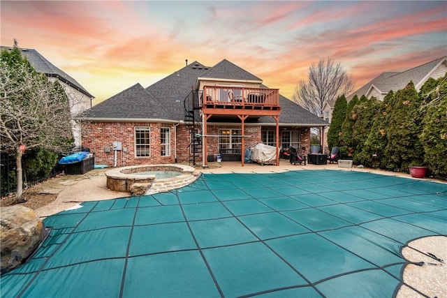 pool at dusk featuring a patio and an in ground hot tub