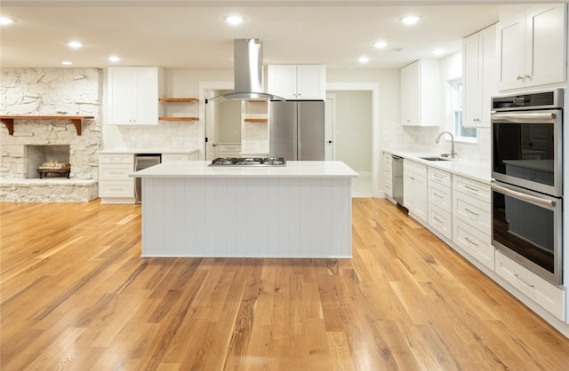 kitchen with island exhaust hood, appliances with stainless steel finishes, a kitchen island, and white cabinets