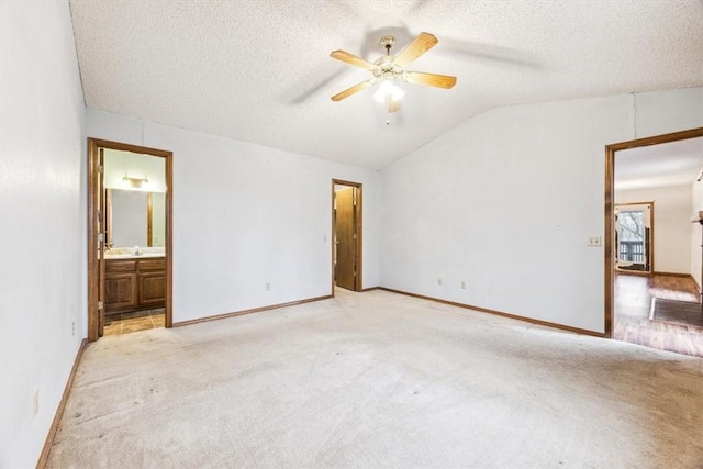 unfurnished bedroom featuring vaulted ceiling, light colored carpet, a textured ceiling, and ensuite bath