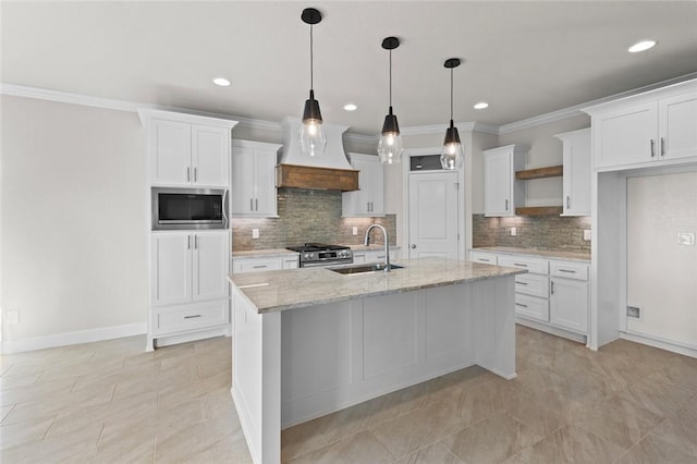 kitchen featuring sink, appliances with stainless steel finishes, white cabinetry, light stone counters, and an island with sink