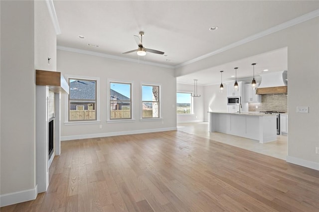 unfurnished living room with crown molding, ceiling fan, sink, and light hardwood / wood-style floors