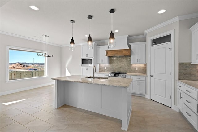 kitchen with sink, appliances with stainless steel finishes, white cabinetry, custom range hood, and an island with sink