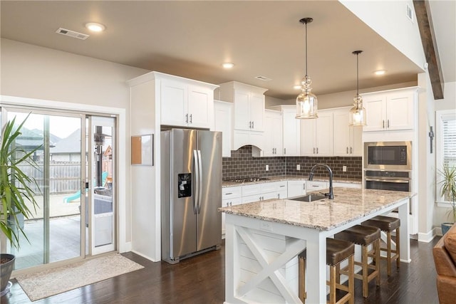 kitchen featuring appliances with stainless steel finishes, white cabinetry, sink, hanging light fixtures, and a center island with sink