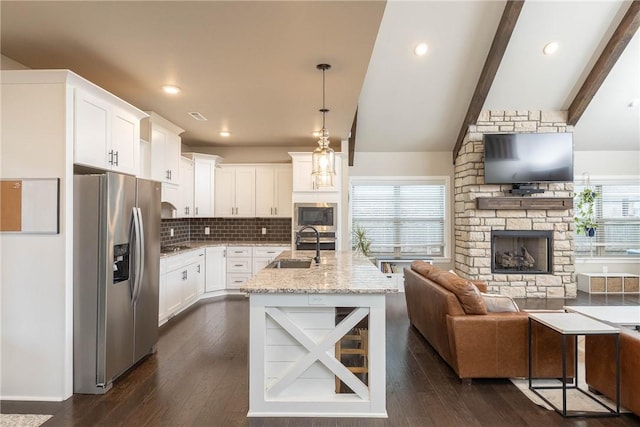 kitchen featuring stainless steel refrigerator with ice dispenser, built in microwave, sink, decorative light fixtures, and light stone countertops