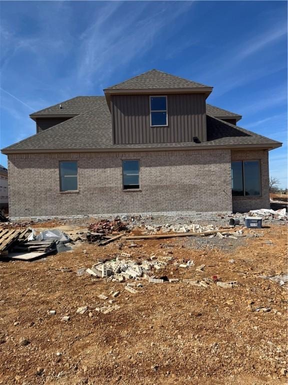 rear view of house featuring brick siding and roof with shingles