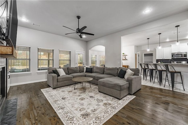 living area with a ceiling fan, visible vents, arched walkways, and dark wood-style flooring