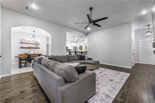 living room featuring ceiling fan with notable chandelier and dark wood-type flooring