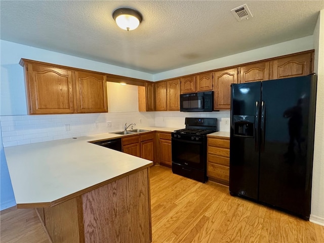 kitchen with black appliances, light wood-style flooring, a sink, a peninsula, and light countertops