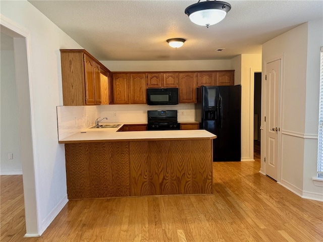 kitchen featuring brown cabinets, black appliances, light wood-style flooring, a sink, and light countertops