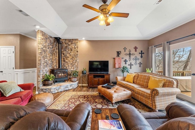 living room featuring crown molding, ceiling fan, hardwood / wood-style floors, a tray ceiling, and a wood stove