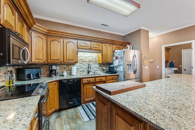 kitchen with sink, light wood-type flooring, light stone countertops, stainless steel appliances, and washer and clothes dryer