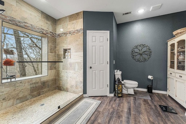 bathroom featuring a tile shower, hardwood / wood-style floors, and toilet