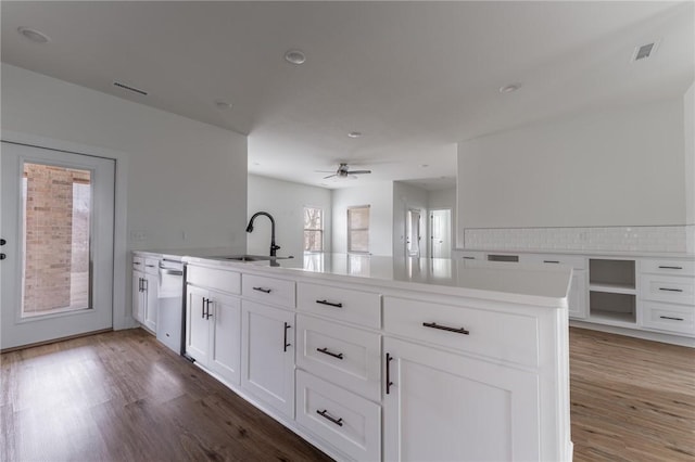 kitchen with sink, white cabinets, hardwood / wood-style flooring, stainless steel dishwasher, and a center island with sink