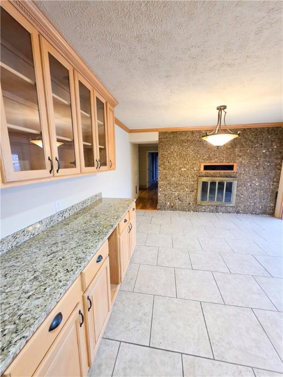 kitchen featuring light tile patterned floors, light stone counters, ornamental molding, a textured ceiling, and brick wall