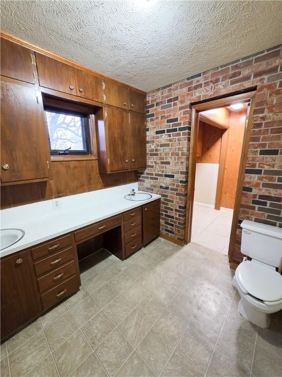 bathroom featuring brick wall, toilet, vanity, and a textured ceiling