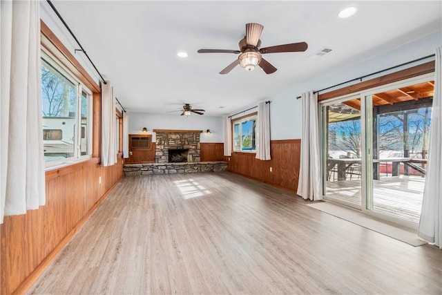 unfurnished living room with wooden walls, a fireplace, a wall mounted AC, ceiling fan, and light hardwood / wood-style floors