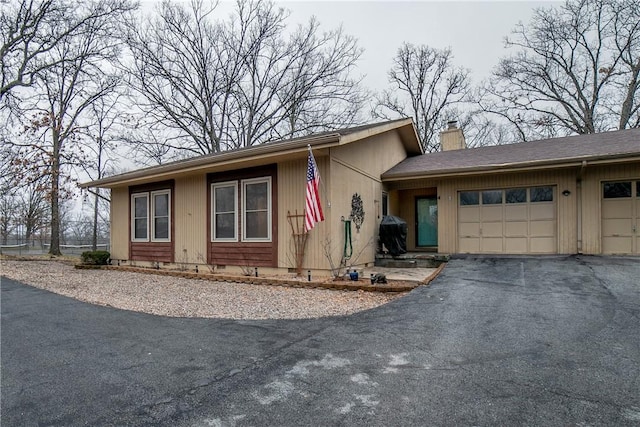 view of front of house with a garage, crawl space, a chimney, and aphalt driveway