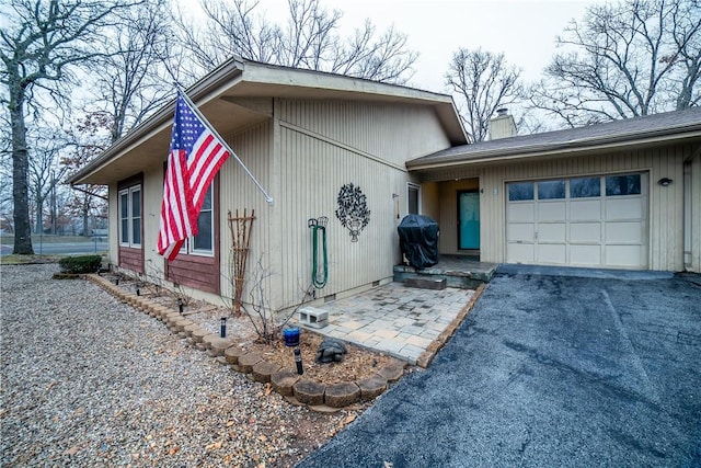 view of front of house featuring driveway, a garage, and a chimney