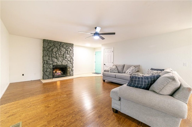 living room with a stone fireplace, wood finished floors, visible vents, a ceiling fan, and baseboards