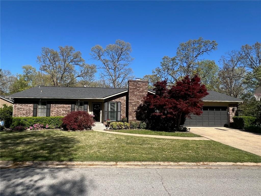 single story home featuring a garage, a chimney, concrete driveway, a front lawn, and brick siding