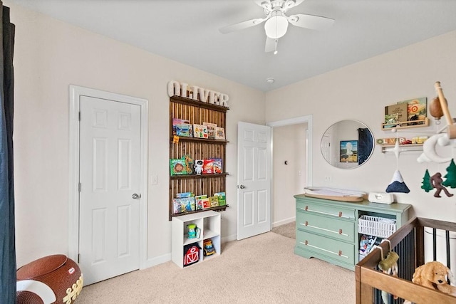 bedroom featuring light carpet, a crib, baseboards, and ceiling fan