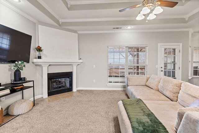 living room featuring a tray ceiling, ornamental molding, ceiling fan, a fireplace with flush hearth, and baseboards