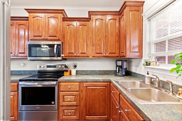 kitchen with stainless steel appliances, a sink, brown cabinetry, and ornamental molding