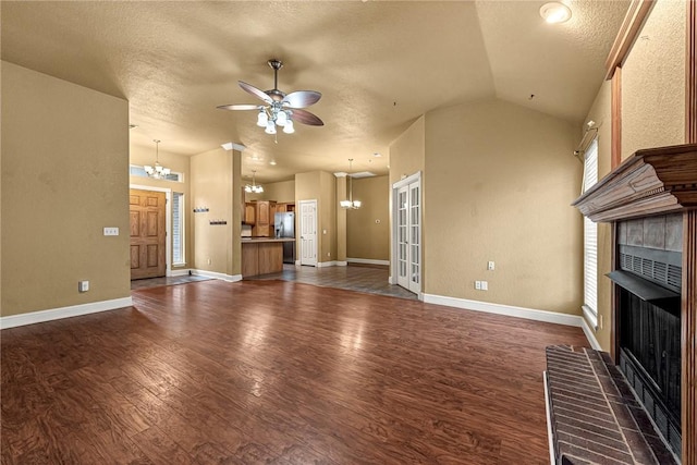 unfurnished living room with dark wood-type flooring, vaulted ceiling, a brick fireplace, a textured ceiling, and ceiling fan with notable chandelier