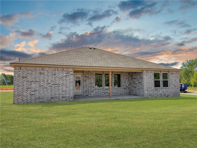 back house at dusk featuring a lawn