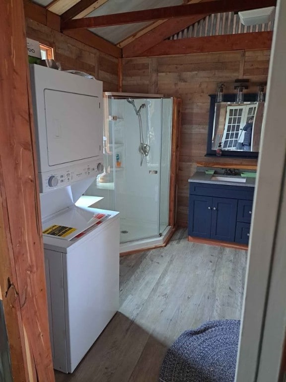 washroom with stacked washer and dryer, sink, hardwood / wood-style floors, and wood walls