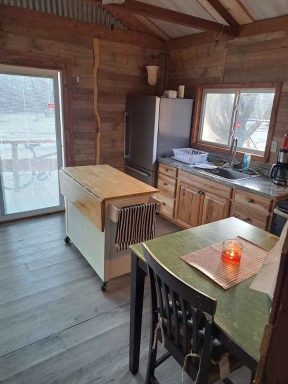 kitchen with a wealth of natural light, wood walls, lofted ceiling with beams, stainless steel fridge, and light hardwood / wood-style floors