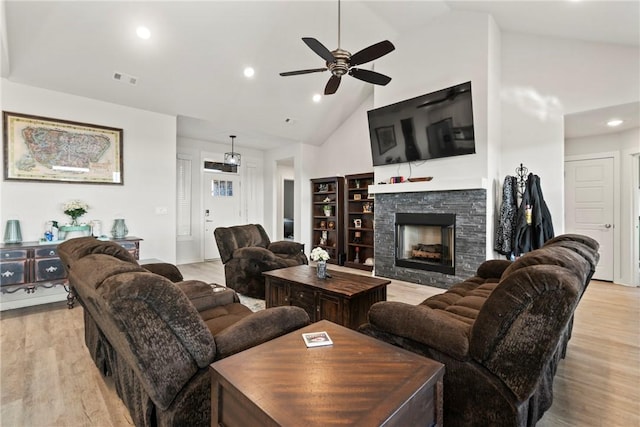 living room with high vaulted ceiling, a stone fireplace, light hardwood / wood-style floors, and ceiling fan