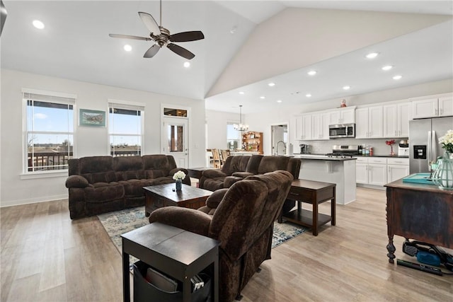 living room featuring sink, ceiling fan with notable chandelier, light hardwood / wood-style flooring, and high vaulted ceiling