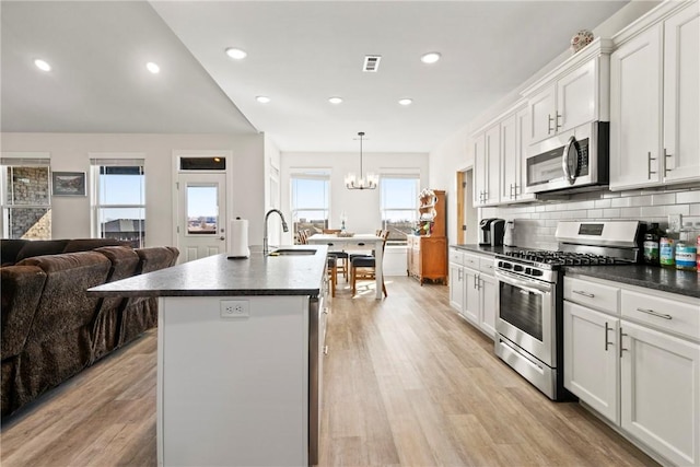 kitchen featuring sink, decorative light fixtures, appliances with stainless steel finishes, an island with sink, and white cabinets