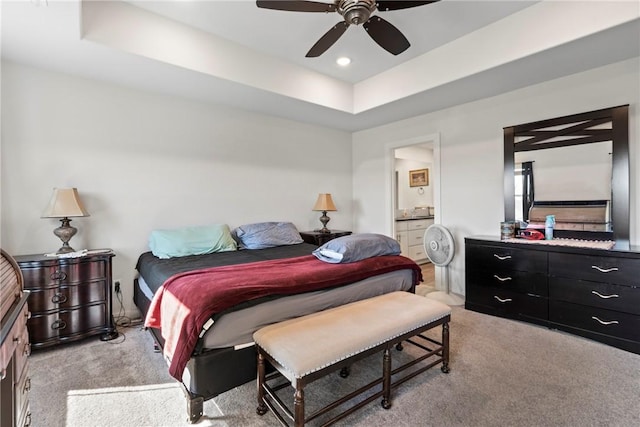 bedroom featuring ceiling fan, ensuite bathroom, a raised ceiling, and light carpet