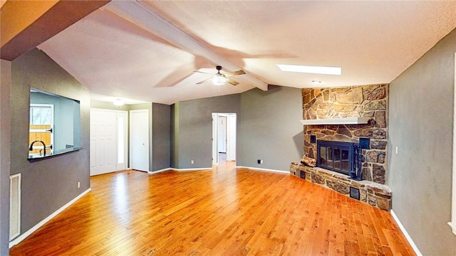 unfurnished living room with lofted ceiling with skylight, hardwood / wood-style floors, ceiling fan, and a fireplace