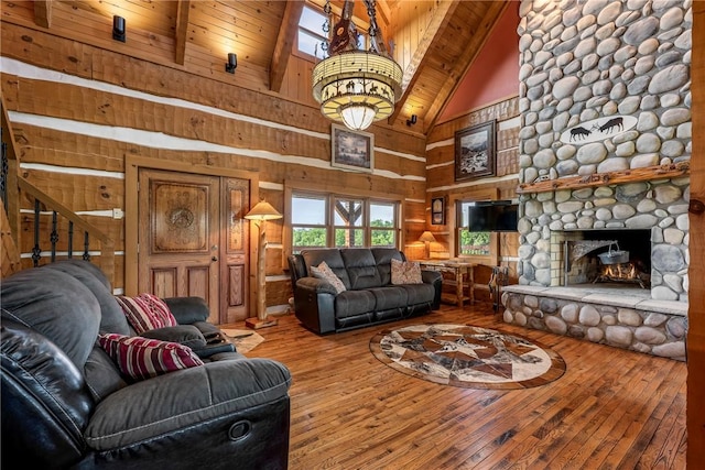 living room featuring a stone fireplace, hardwood / wood-style floors, high vaulted ceiling, wooden walls, and beamed ceiling