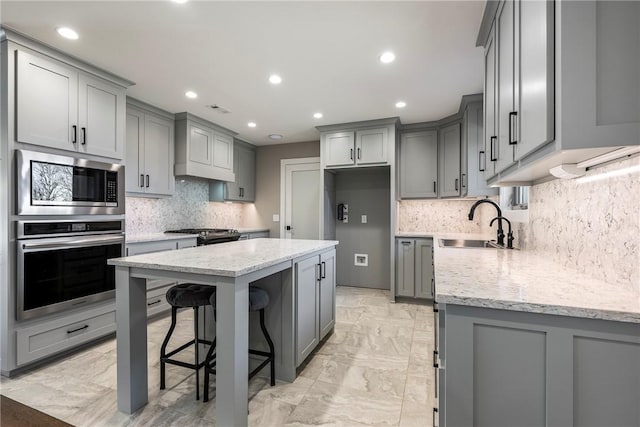 kitchen with sink, gray cabinets, appliances with stainless steel finishes, light stone countertops, and a kitchen island