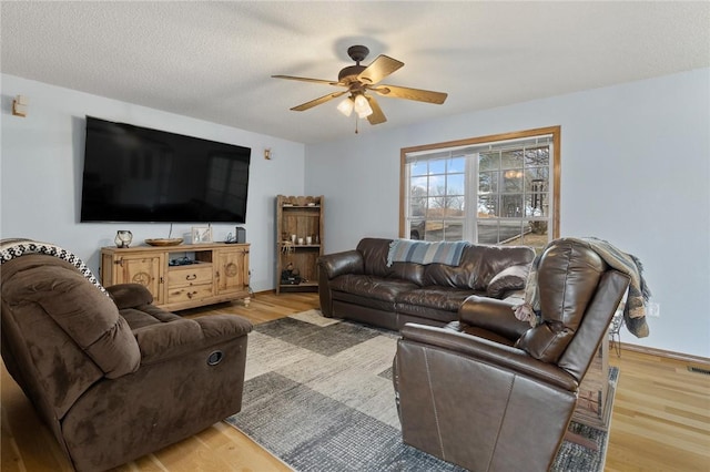 living room with ceiling fan, a textured ceiling, and light wood-type flooring