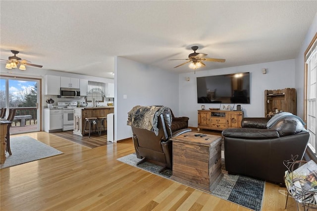 living room featuring ceiling fan, sink, a textured ceiling, and light wood-type flooring