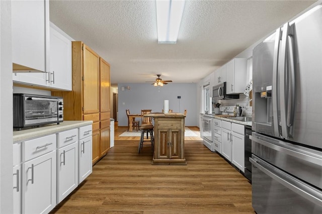 kitchen with dark hardwood / wood-style floors, a breakfast bar area, white cabinets, ceiling fan, and stainless steel appliances