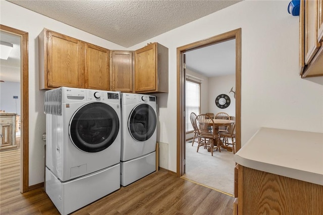 laundry room with cabinets, wood-type flooring, washer and dryer, and a textured ceiling