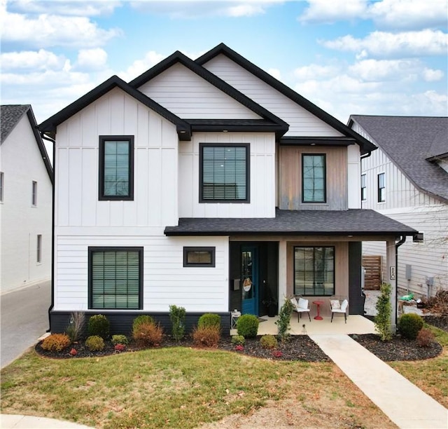 modern farmhouse featuring roof with shingles, a porch, board and batten siding, and a front yard