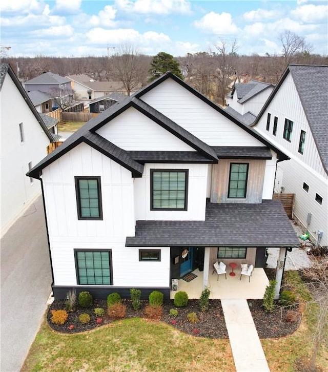 modern farmhouse style home with a patio, roof with shingles, a residential view, a front lawn, and board and batten siding