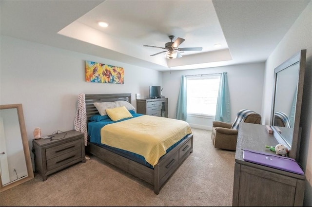 bedroom with light carpet, a tray ceiling, and ceiling fan