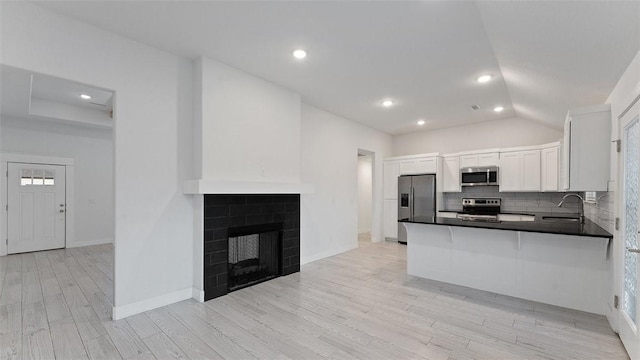 kitchen featuring light wood finished floors, a sink, appliances with stainless steel finishes, dark countertops, and backsplash