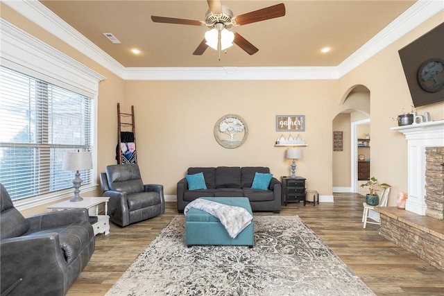 living room featuring hardwood / wood-style flooring, a stone fireplace, ornamental molding, and ceiling fan